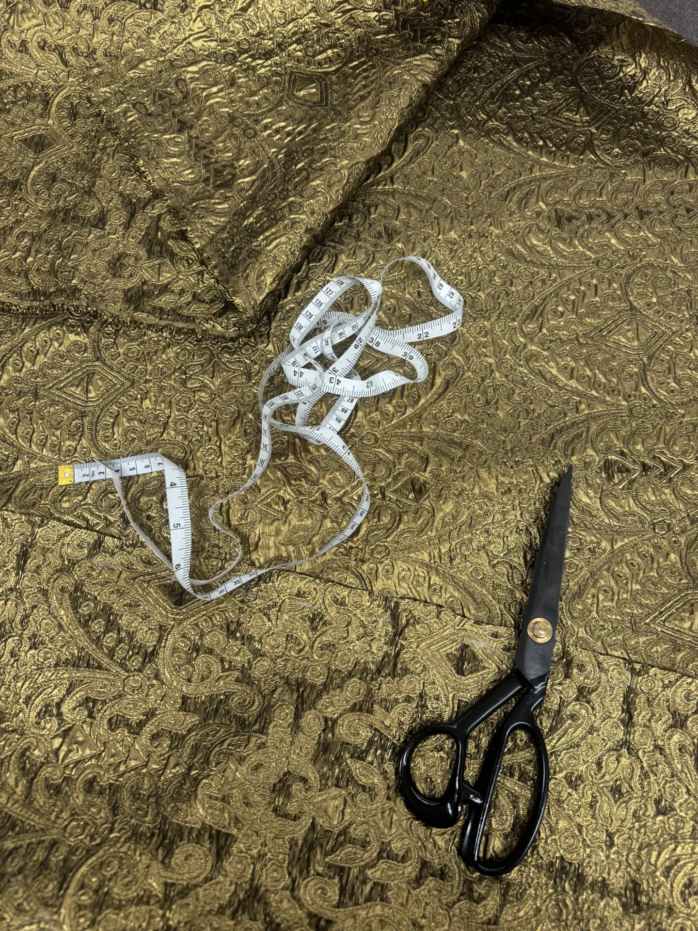 Gold brocade cloth on the cutting table with a tailor's tape measure and shears