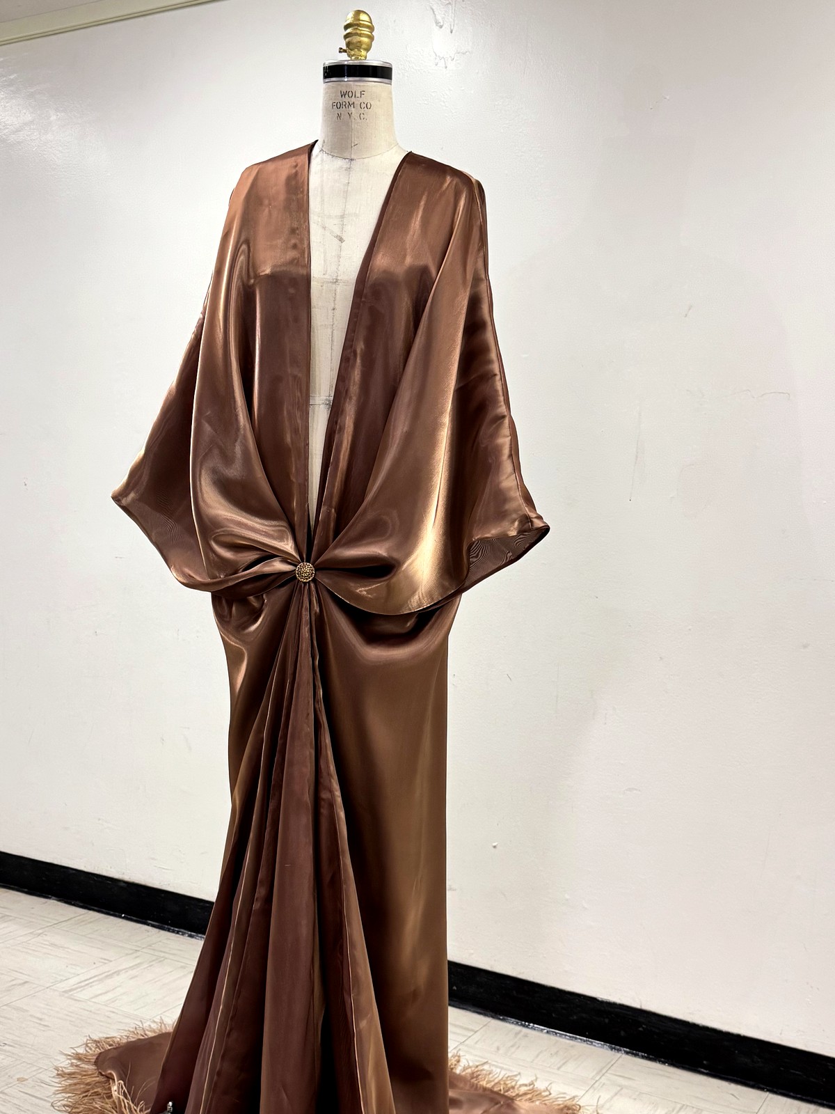 Bronze silk satin cape gown with ostrich feather hem on an atelier stand